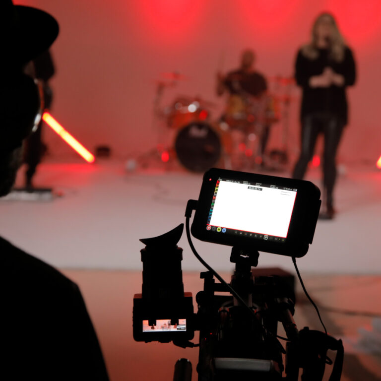 Making-of beim Musikvideo-Dreh der Band Radiant – Kamera im Vordergrund filmt die Band im Studio mit roter Beleuchtung