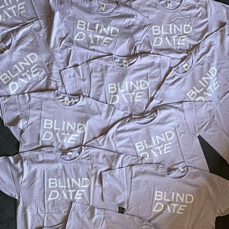 Mehrere lilafarbene T-Shirts mit weißem „Blind Date“-Logo für die Filmcrew