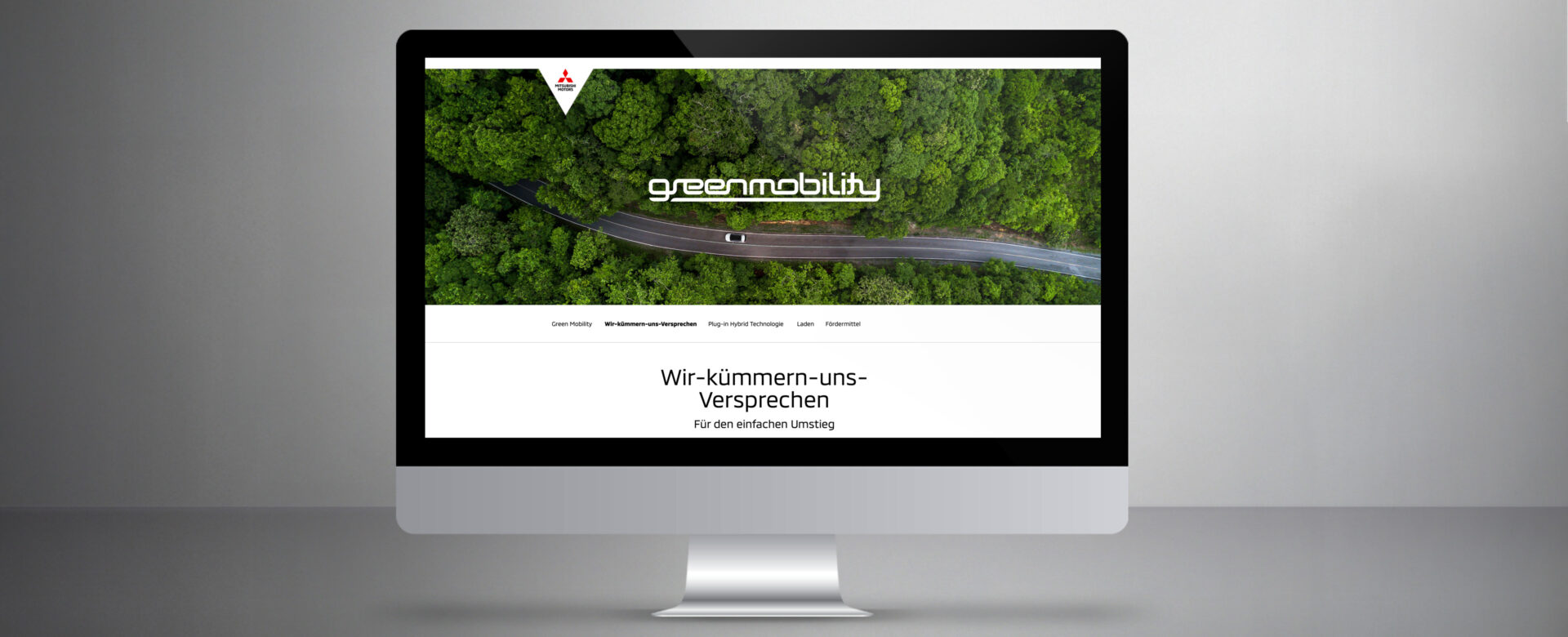 Desktopansicht der Mitsubishi Green Mobility Website mit Luftaufnahme einer Straße durch grünen Wald und dem Claim „Wir-kümmern-uns-Versprechen – Für den einfachen Umstieg“
